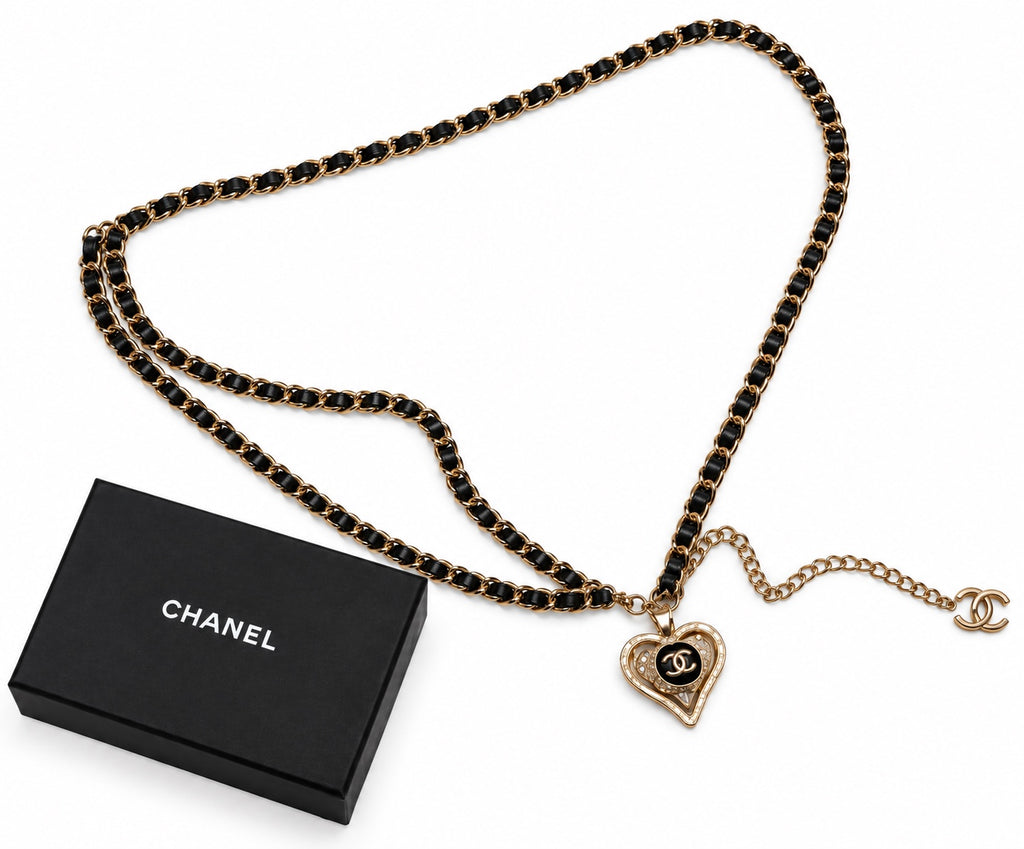 חגורת שרשרת Chanel בגוון זהב עם עור שחור שזור, תליון לב ולוגו CC לצד קופסת Chanel